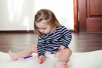 little girl draws on the floor in a room on a sunny day