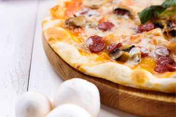 Closeup of hot homemade pizza with sausage, mushrooms, mozzarella cheese and basil on wooden board ready to eat, copy space. Italian traditional cuisine. Delicious italian food, shallow depth of field