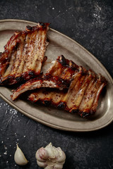 Closeup shot of flavorful grilled pork ribs in thick barbeque sauce cut in messy way served in vintage metal tray on dark textured background. Pub styling concept.