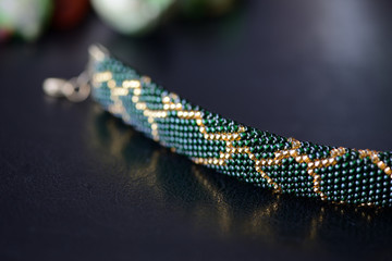 Dark green beaded necklace with golden print on a dark background close up