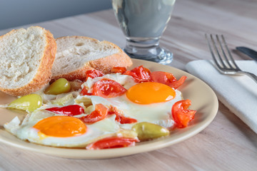 Freshly cooked scrambled eggs with fried cherry tomatoes and chili peppers on a plate. Serving.
