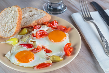 Freshly cooked scrambled eggs with fried cherry tomatoes and chili peppers on a plate. Serving.