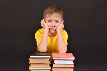 A boy with books. A schoolboy teaches lessons. Shooting in a studio. A child in a yellow T-shirt. A smart person. A commitment to knowledge.