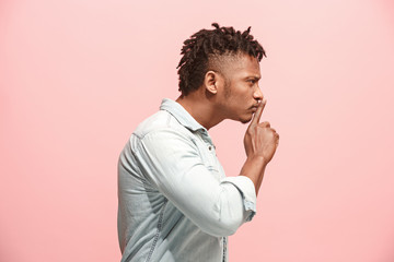 The young man whispering a secret behind her hand over pink background