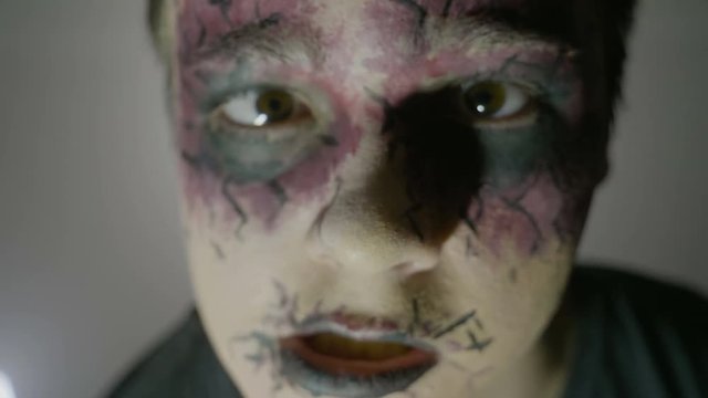 Close up of a young boy wearing halloween zombie face paint makeup and costume looking straight to camera