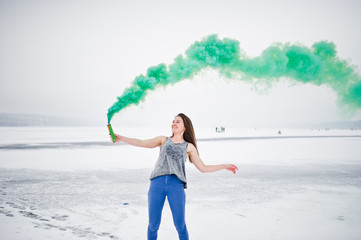 Young girl with green colored smoke bomb in hand in winter day.