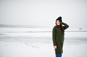 Fototapeta na wymiar Funny girl wear on long green sweatshirt, jeans and black headwear, at frozen lake in winter day.