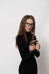 Fototapeta premium Beautiful girl with glasses. The book in the hands. Black dress. White background.