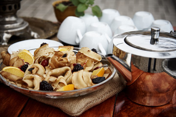 Pancakes with fresh berries in a glass plate stand on a wooden table with a samovar and mugs in the fresh air.