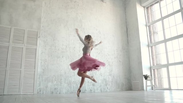 The ballet dancer is spinning in a classic tutu and pointe shoes. A young ballerina dances on tiptoe against the background of a large light window