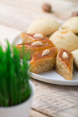 Traditional Azerbaijan Novruz table decoration setting for spring equinox new year celebration, white plate with shekerbura and pakhlava, various size wheat grass symbol Nowruz, close up copy space