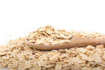 Pile of organic oat flakes and full fill in the wooden spoon on white background.
