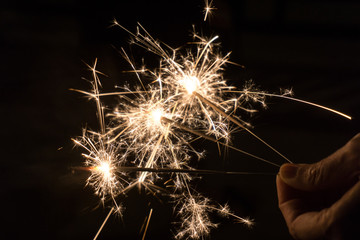 Hand holding golden sparklers shining  in the dark at nigh for birthday party and celebrate new year.