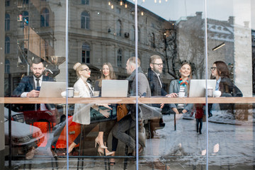 Business people during the coffee break sitting with laptops near the window. View through the window with city reflection