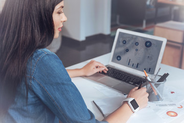 Fototapeta premium Have an idea. Attractive freelancer sitting in semi position and making notes while analyzing diagram