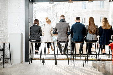 Back view on the business people sitting in a row near the window in the cafe