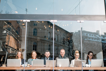 Business people during the coffee break sitting with laptops near the window. View through the...