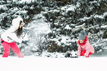 Young woman and her baby throwing snow, happy and fun