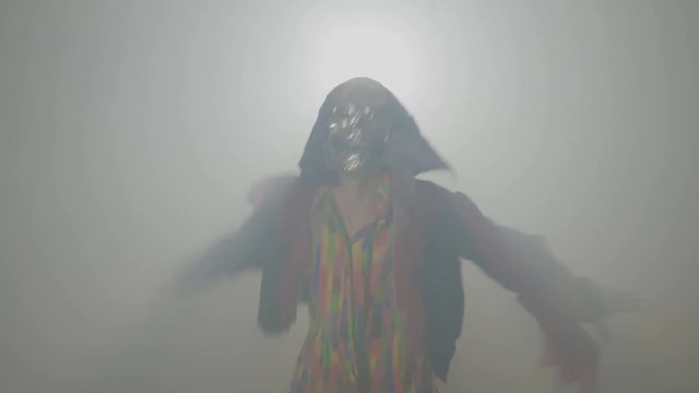 Malefic evil creature wearing a mask and doing the funny zombie dance in fog on halloween night