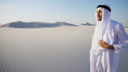 Smart handsome emirate Arabian UAE Sheikh businessman prints on computer keyboard and answers incoming phone call from business partner or client, communicates about building in desert. Young Arab