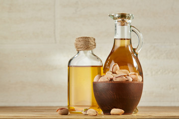 Fototapeta na wymiar Aromatic oil in a glass jar and bottle with pistachio in bowl on wooden table, close-up
