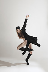 Young beautiful dancer in beige swimsuit dancing on gray background