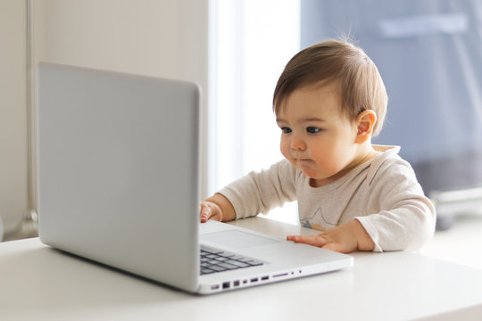 little baby is looking attentively at the screen of laptop in front of him, working with computer.  Child and computer concept