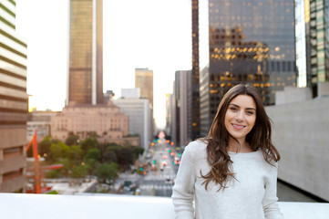 Beautiful young woman sitting on a bridge across the boulevard in urban scenery, downtown, at sunsetm smiling spontaneous.
