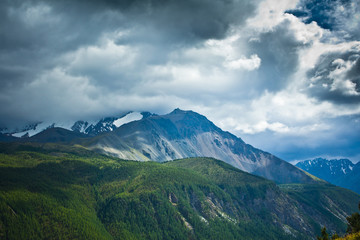 Beautifull  view to snow mountains and green field with sunlight and sky in the storm