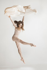 Young beautiful dancer in beige swimsuit dancing on gray background