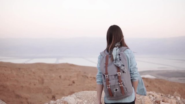 Woman takes photos of montain scenery. Slow motion. Casual traveler girl with backpack using smartphone. Israel Dead Sea
