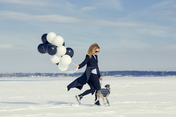 A woman with balloons and a dog of the Italian Greyhound breed has fun in the winter on snow, in the winter.