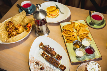 Pancakes with chocolate, salmon fish and tea kettle on table in cafe. Table with tasty food.