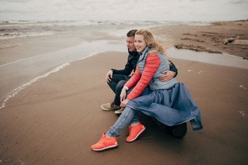 happy young couple sitting on log and looking at Baltic sea in Riga