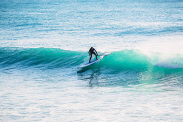 Surfer on stand up paddle board on wave. Winter surfing in ocean
