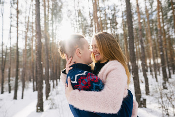 side view of happy young couple hugging and smiling each other in winter forest