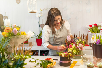 Obraz na płótnie Canvas Smiling woman florist, small business flower shop owner, at counter, working at a special flower arrangement.