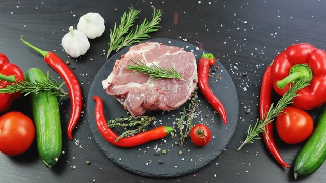 close up view of adding salt and spices to raw piece of meat beef steak with fresh juicy vegetables. herbs cucumber pepper tomatoes marinating professional cooking master kitchen ecology nutrition
