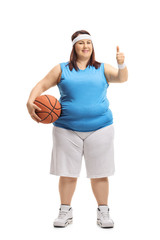 Overweight woman in sportswear holding a basketball and making a thumb up sign