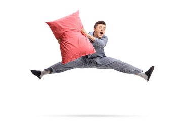 Overjoyed teenager in pajamas holding a pillow and jumping