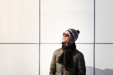 Young man outdoors smiling. Male teenager person stands at minimalistic background in casual winter clothes and sunglasses and smiles cheerfully