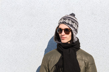 Stylish male teenager. Handsome young man in sunglasses and knitted hat poses outdoors on cold sunny winter day