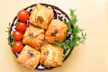 delicious Uzbek pieces of samos with cherry tomatoes, chili on a plate with Uzbek ornament on a beige rustic background for breakfast, space for text