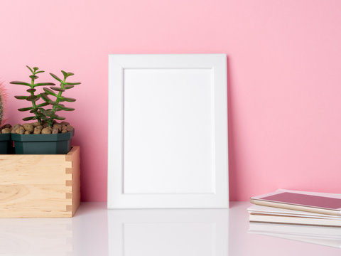 Blank white frame and plant cactus on a white table against the pink wall with copy space. Mockup with copy space.
