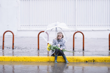 little girl sitting in the street with a bouquet of flowers in rain day and  umbrella
