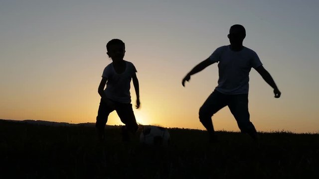 Father and son playing soccer in the park at the sunset time. People having fun outdoors. Concept of friendly family. 