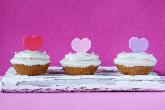 Three homemade raw capkake with cashew cream on a pink background