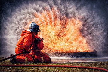 Firefighter in fire fighting suit spraying water, Firemen fighting  raging fire with huge flames of...