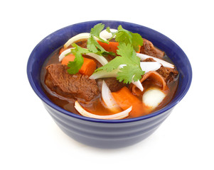 beef stew and vegetables in blue bowl on white background