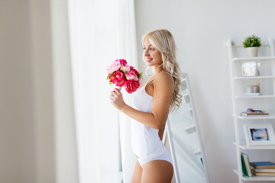 woman in underwear with bunch of flowers at window